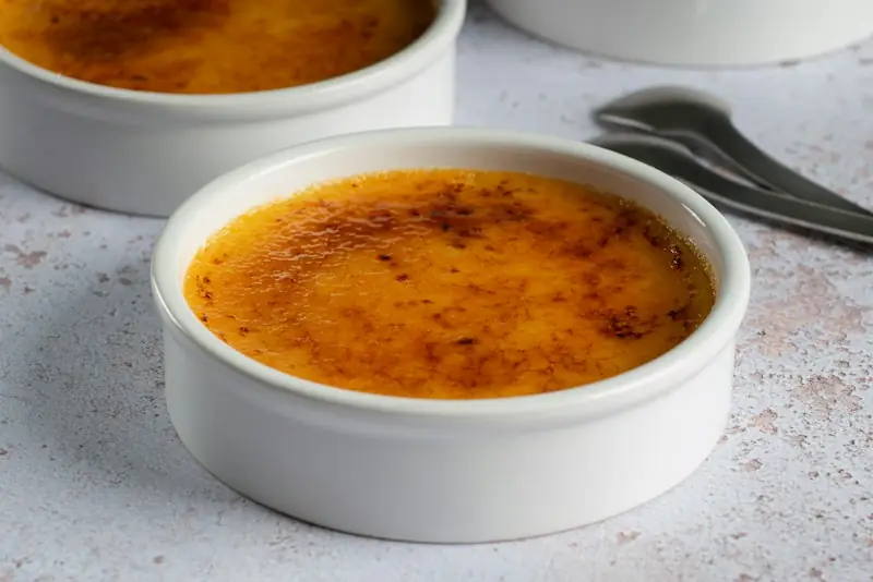 Crème brûlée em ramequins brancos, com a casquinha de açúcar queimado por cima e colheres ao lado
