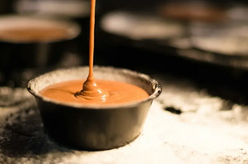 Fio grosso de caramelo escorrendo para dentro de uma panelinha escura