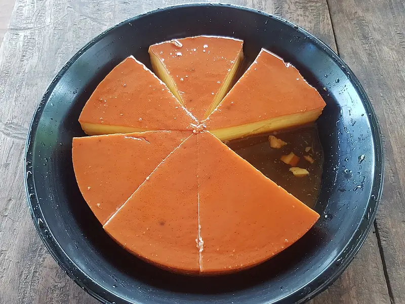 Leche flan filipino cortado em fatias numa travessa preta, alaranjado por cima e amarelo por dentro, com calda no fundo