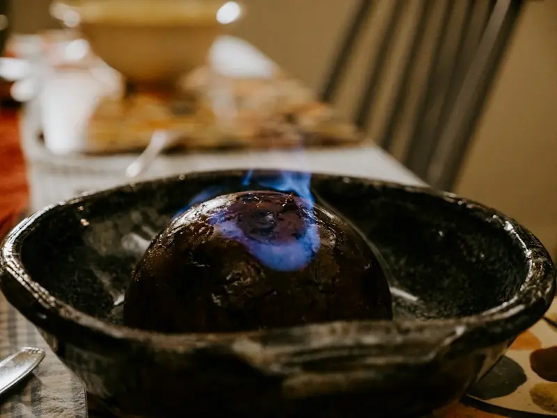 Christmas pudding inglês escuro e redondo pegando fogo com chama azul numa tigela de cerâmica