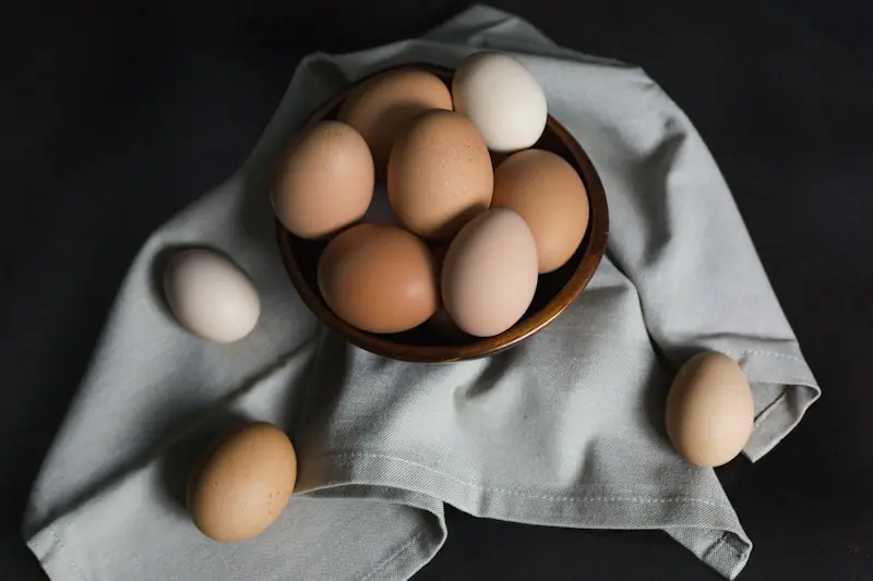 Ovos de casca bege e branca numa tigela de madeira sobre um pano cinza