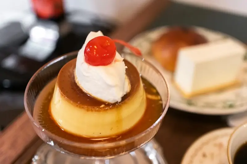 Purin japonês numa taça de vidro, com chantili e uma cereja em calda por cima