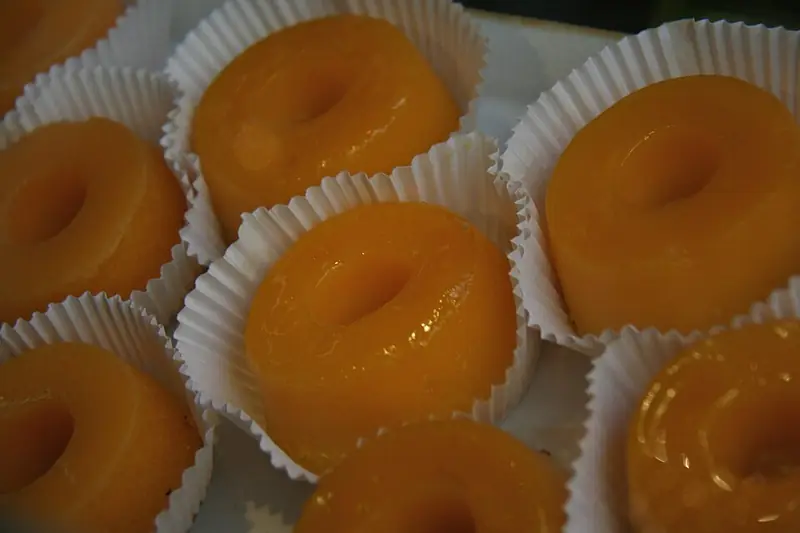 Quindins amarelo-alaranjados e brilhantes, com furo no meio, cada um numa forminha de papel branca