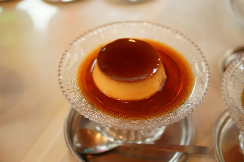 Pudim pequeno numa taça de vidro lapidado, mergulhado em calda de caramelo escura